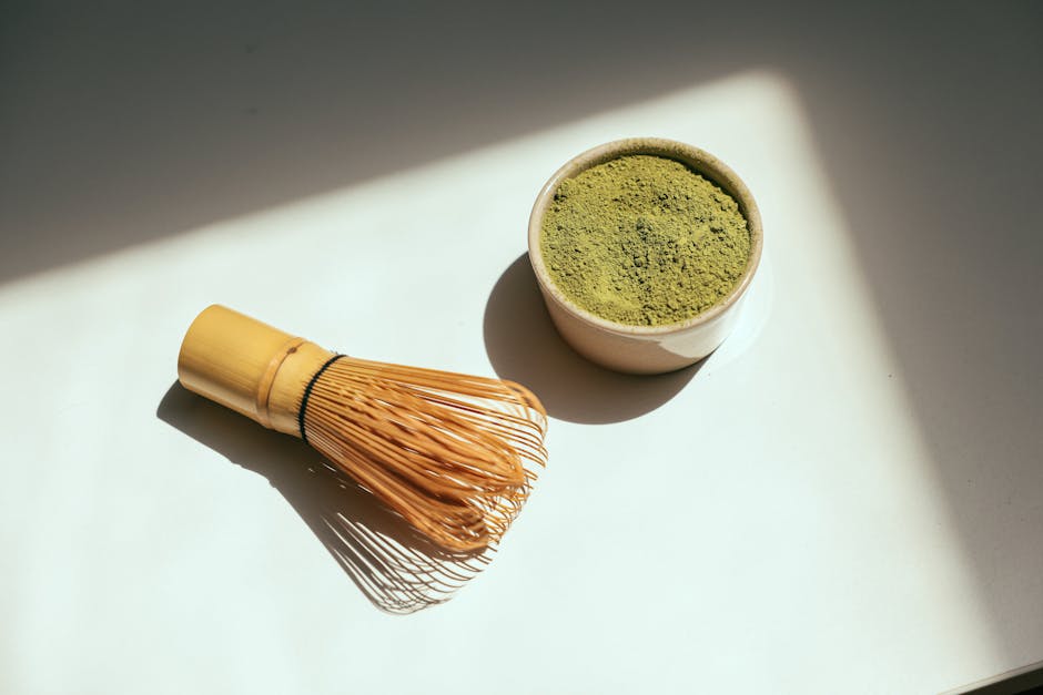 Matcha green tea powder in a bowl with bamboo whisk
